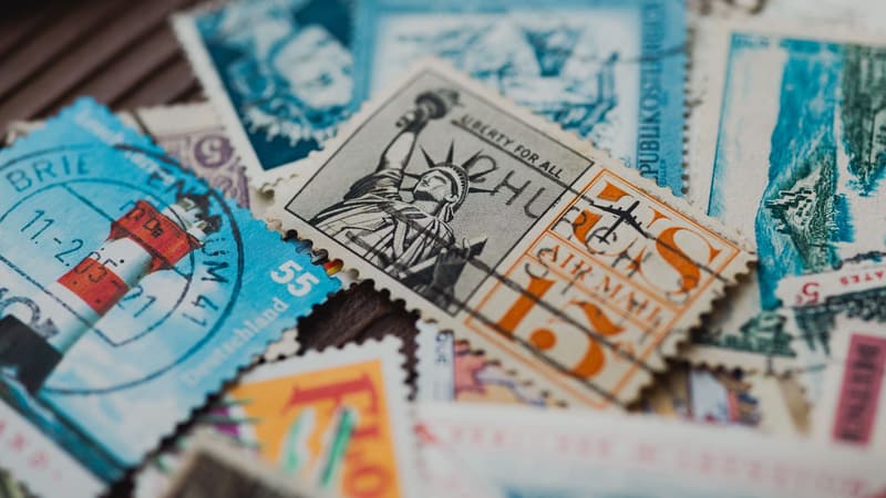 A scatter of hand-stamped envelopes, collage fragments, and postcards arranged on a sunlit wooden desk