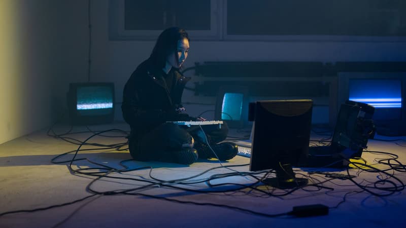 A lone spotlight illuminating an empty chair on a dark stage, with blurred scattered phone screens glowing faintly in the background like a distant audience